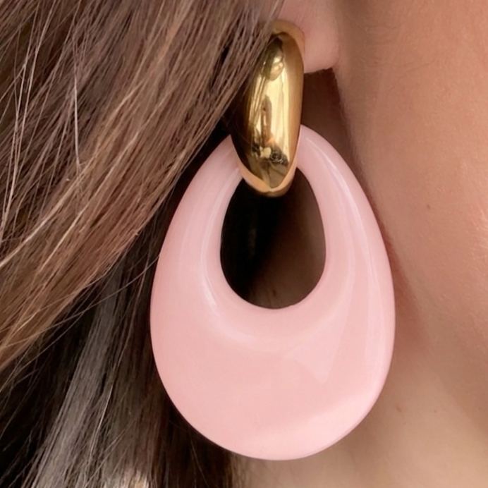 Boucles d'oreilles pendantes Maya en acier inoxydable doré et résine rose poudré portées par une femme.